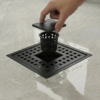 A hand lifting the removable 304 stainless steel hair catcher basket from a Veloaura matte black square shower drain to prevent clogs.