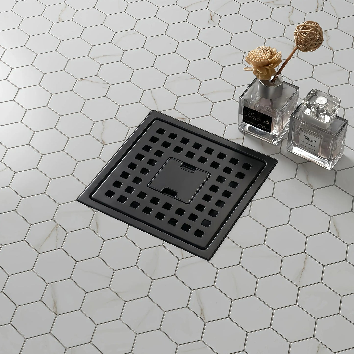 Veloaura 6 inch 304 stainless steel matte black square shower drain installed on a modern bathroom floor with marble hexagon mosaic tiles.