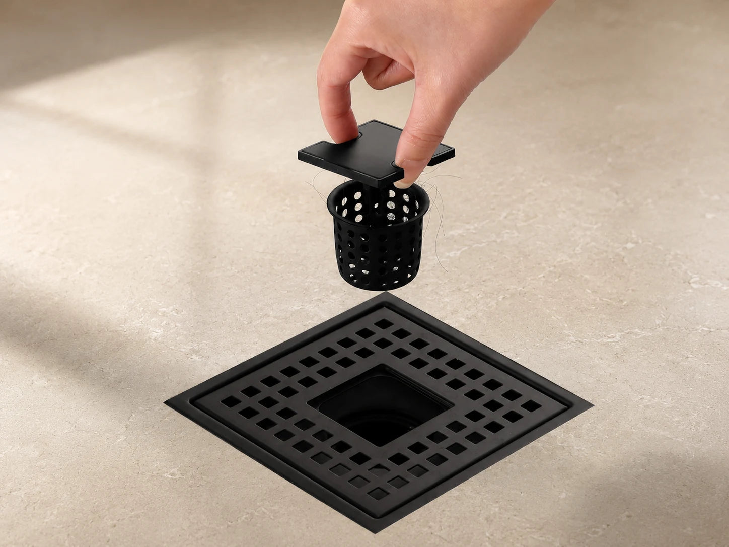 Veloaura matte black square shower drain with lift-out hair catcher being removed by hand